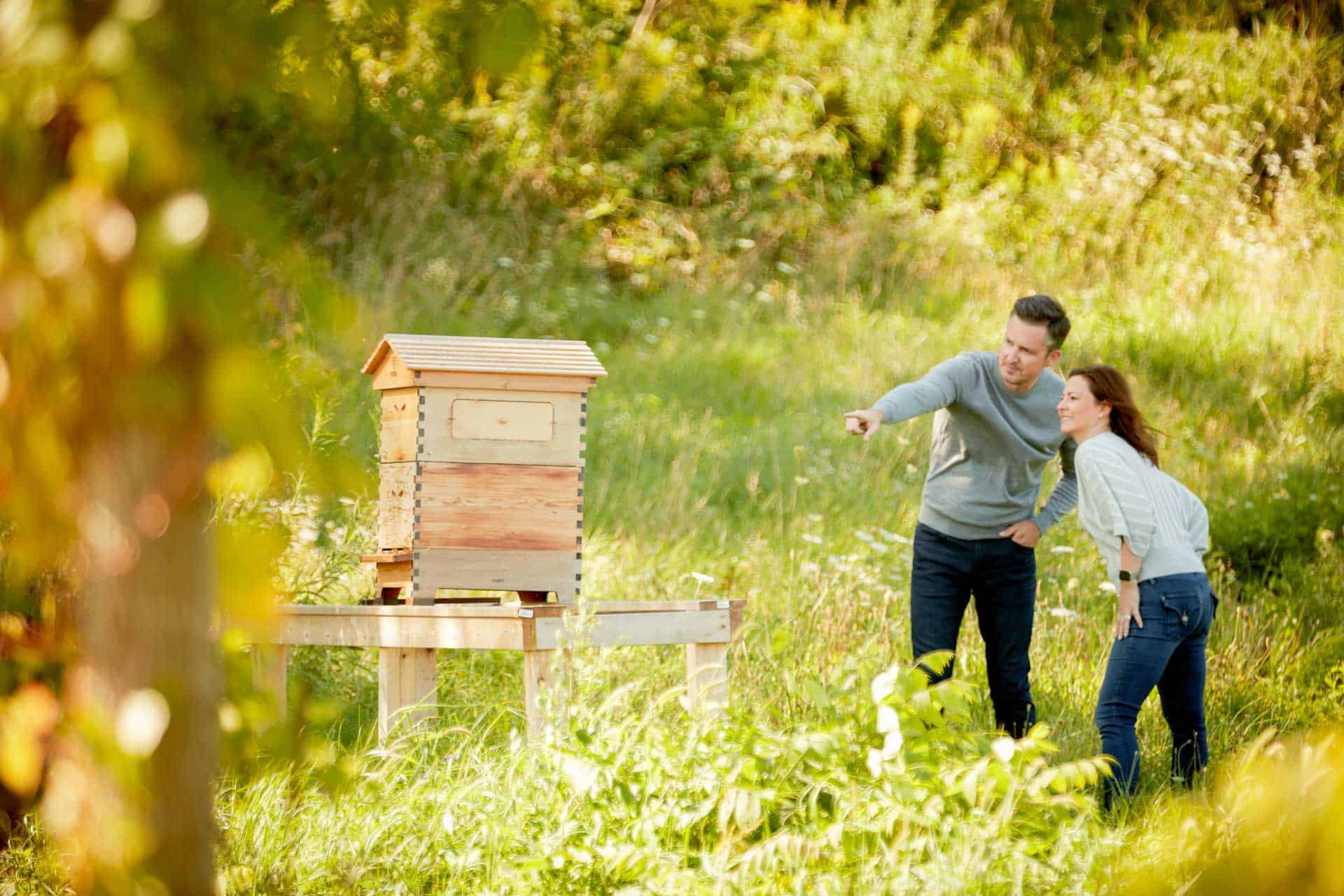 Matt and Melissa standing near a bee box pointing at it